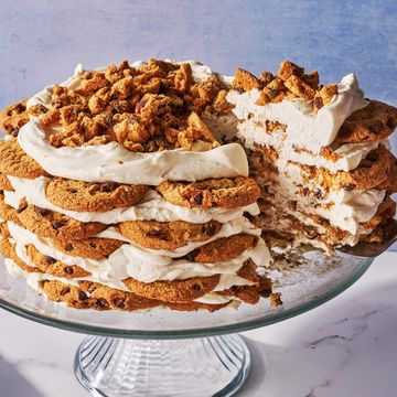 icebox cake made of chocolate chip cookies and whipped cream layered on a cake stand in front of a blue background