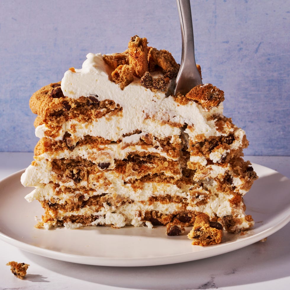 icebox cake made of chocolate chip cookies and whipped cream layered on a cake stand in front of a blue background