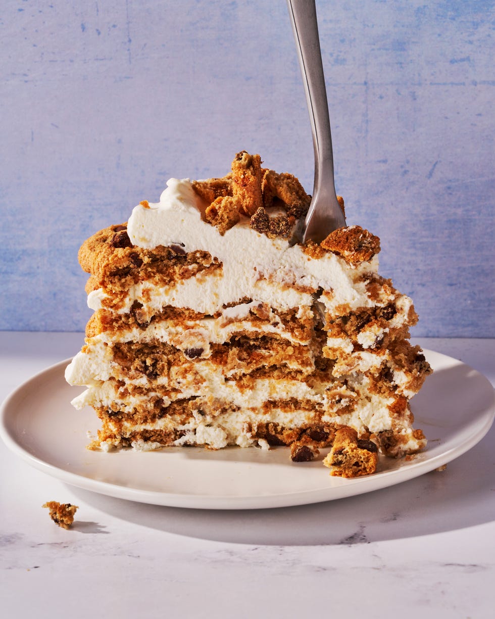 icebox cake made of chocolate chip cookies and whipped cream layered on a cake stand in front of a blue background