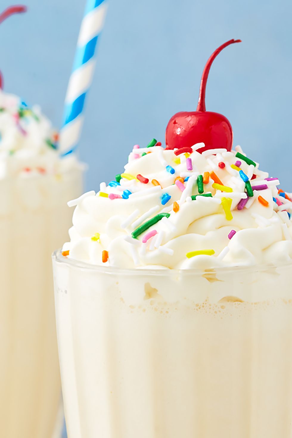closeup of vanilla milkshake topped with rainbow sprinkles and a maraschino cherry
