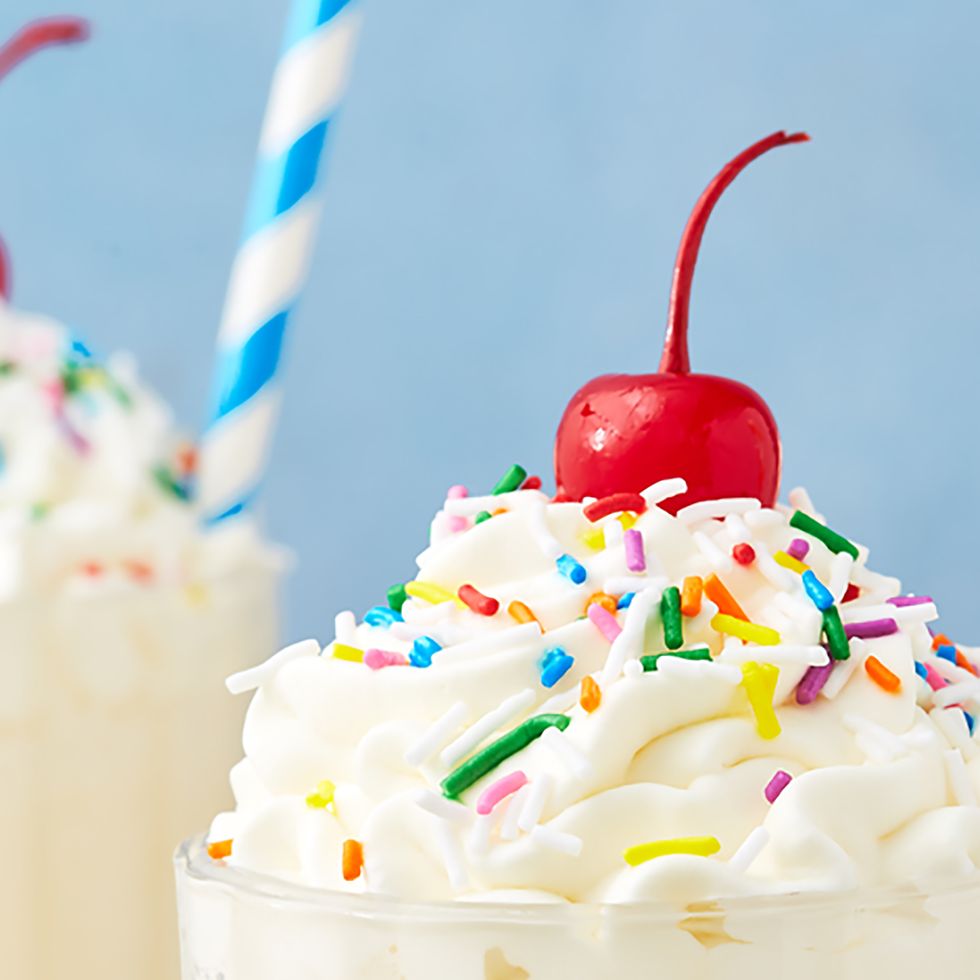 closeup of vanilla milkshake topped with rainbow sprinkles and a maraschino cherry