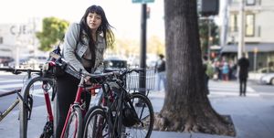 millennial latina bicycle commuting, locking her bike on city sidewalk