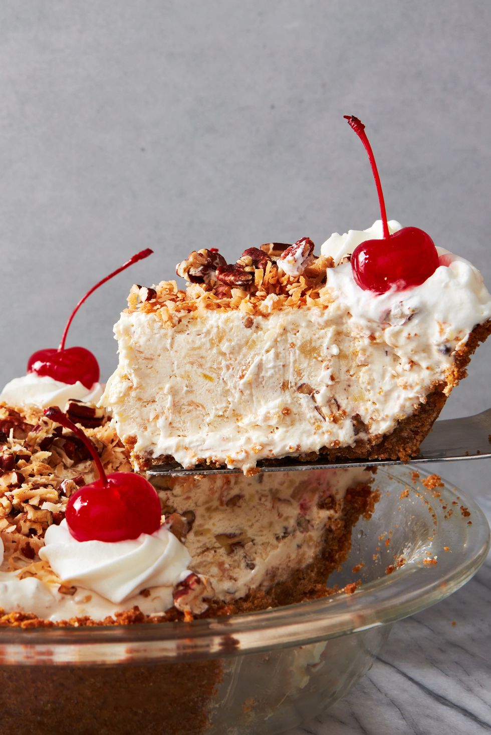 layered pie topped with crushed nuts, whipped cream, and cherries