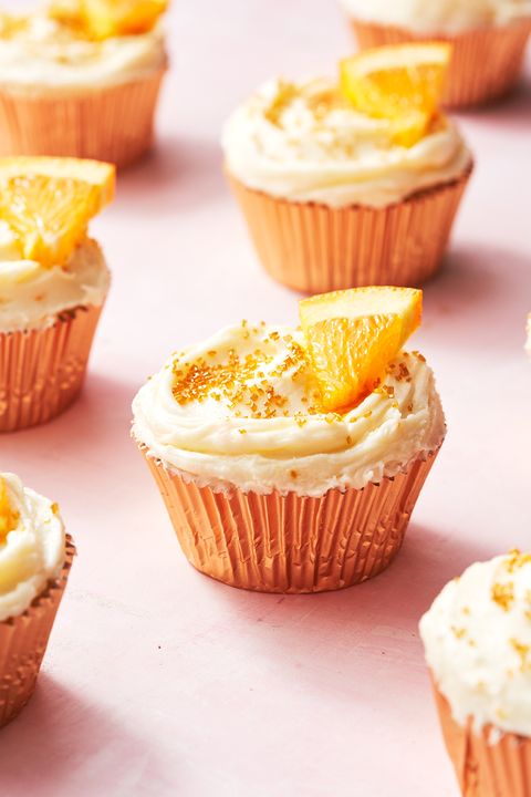 mimosa cupcakes with gold sprinkles and orange wedges on a pink background