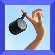 soundcore bluetooth speaker hanging from finger against blue sky and jbl mini speaker clipped to beach beach