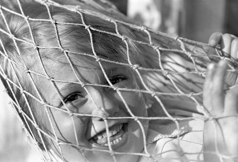Small child smiling through the netting of a hammock, c.1930s.