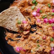 cheesy mini meatball skillet dip in a black cast iron skillet topped with pickled red onions and green scallions with a single tortilla chip
