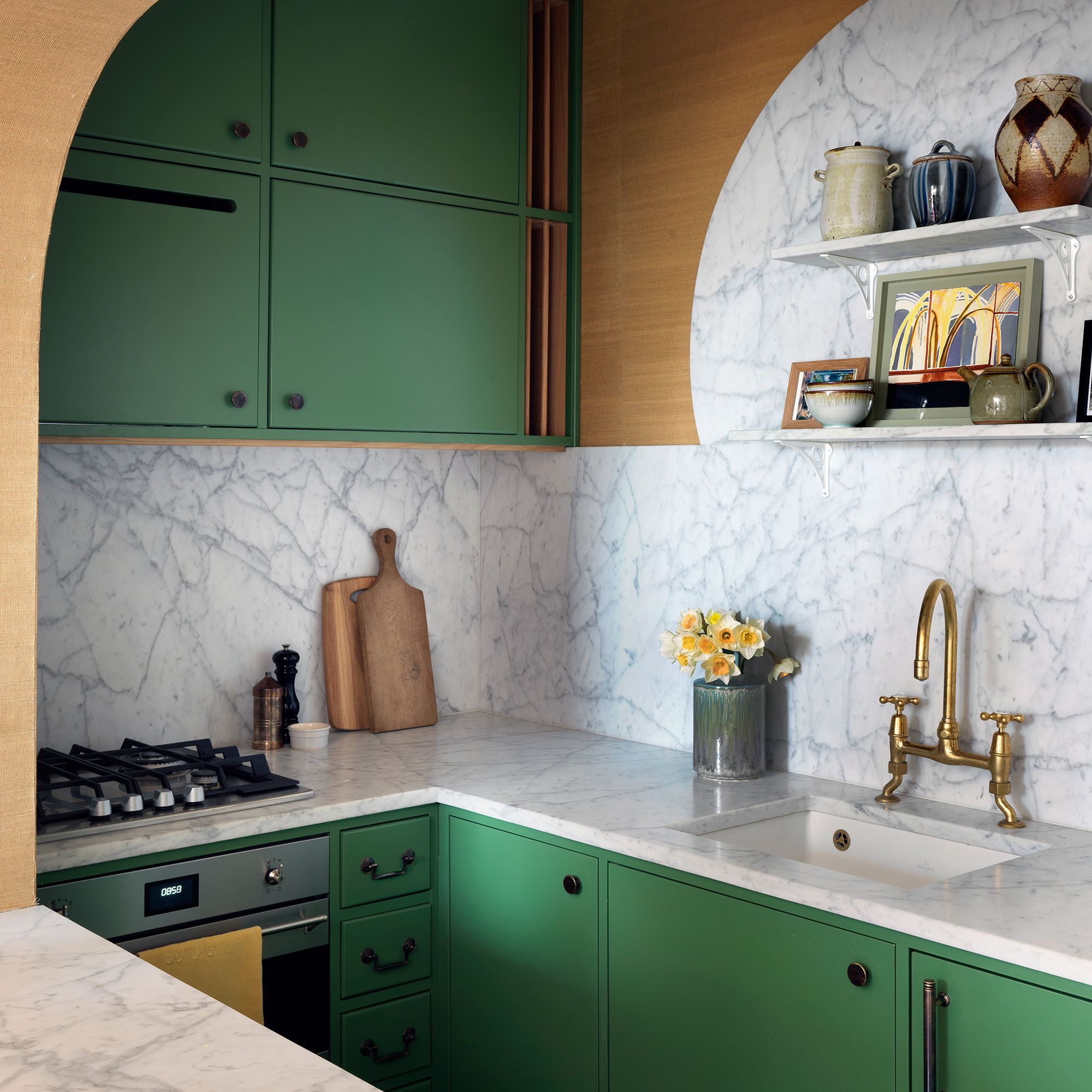 Una cocina con un mueble de cocina verde con tiradores dorados y una  encimera de mármol blanco.