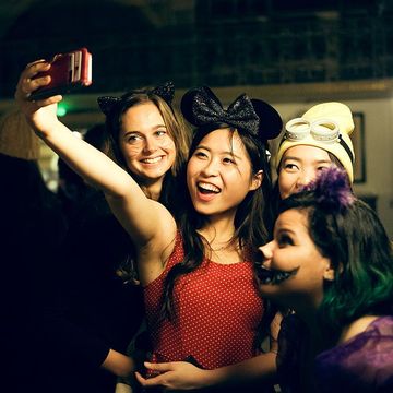 four female students taking a selfie on phone while wearing a minnie mouse costume, cat costume, minion costume and cheshire cat costume