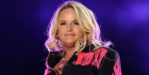 miranda lambert smiles while performing, she wears a black western outfit with pink fringe and embellishments