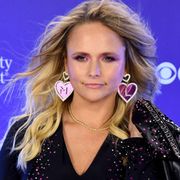 miranda lambert wearing large heart earrings and sequin jumpsuit with a leather jacket thrown over her shoulder