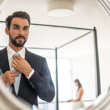 mirror reflection of young businessman adjusting shirt and tie in hotel room, dubai, united arab emirates