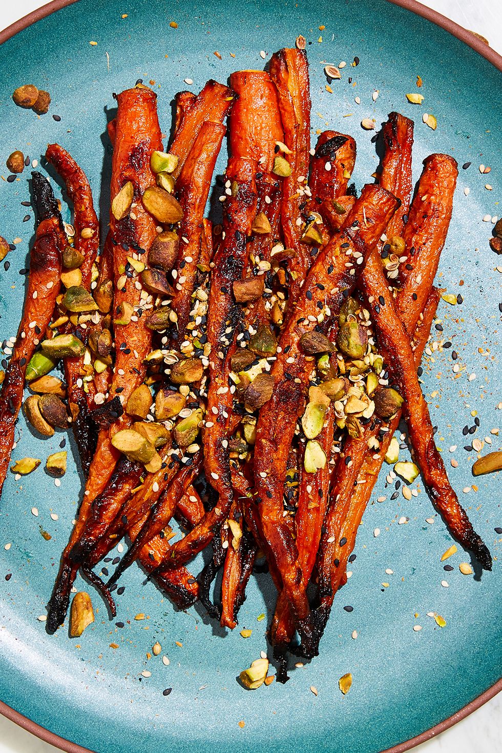 miso glazed carrots topped with pistachios and white and black sesame seeds on a teal plate
