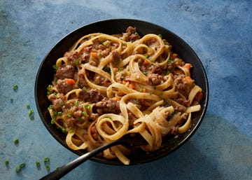 miso fettuccine bolognese garnished with chives in a black bowl on a blue background