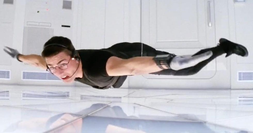 ethan hunt dangles from the ceiling during a break in heist in a scene from mission impossible it is the first film if you're watching the mission impossible movies in order