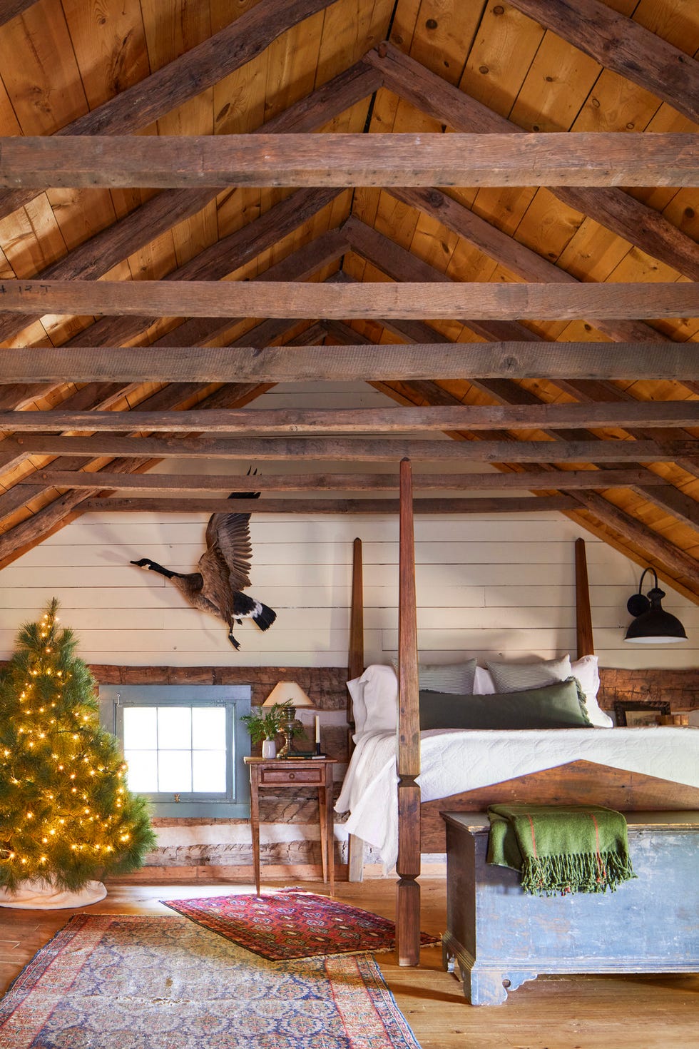 cozy cabin attic bedroom with wood four poster bed, layered turkish rugs, and a small christmas tree