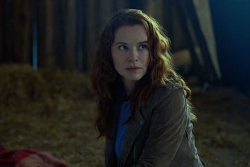 a person seated in a rustic barn setting with straw on the ground