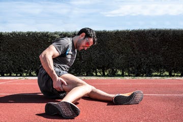 caucasian man in sports clothes, injured on the athletics track, touching his thigh and looking in pain