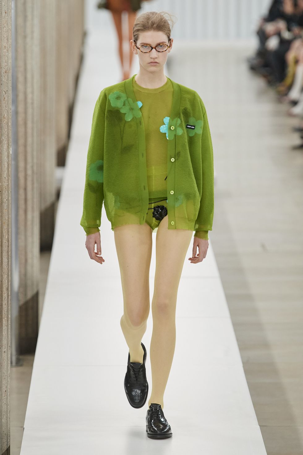 a person wearing a green jacket and black shoes walking down a runway