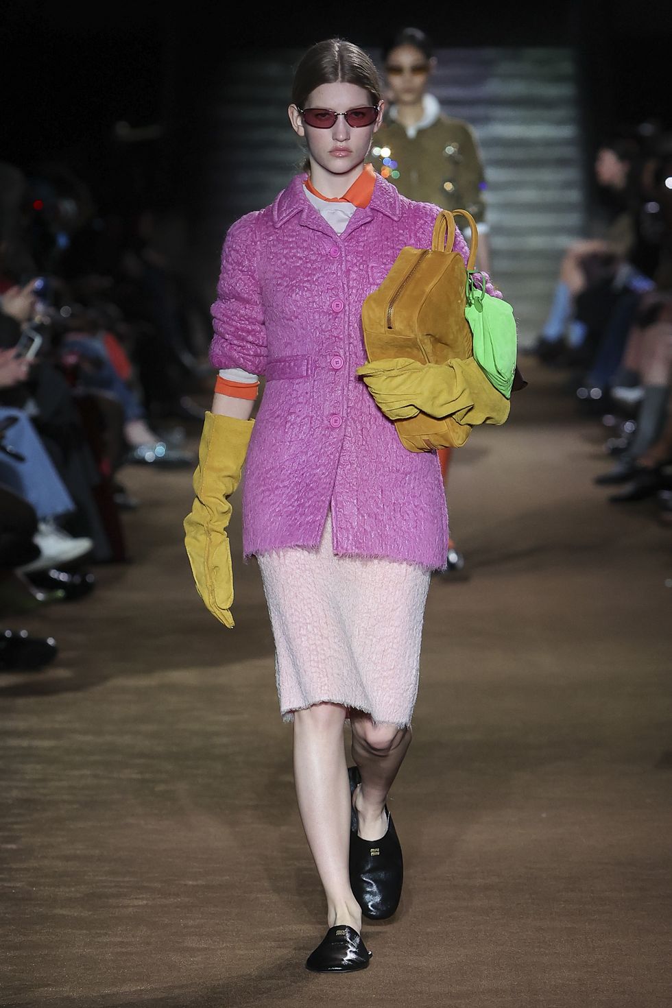 a person wearing a pink coat and sunglasses walking down a runway