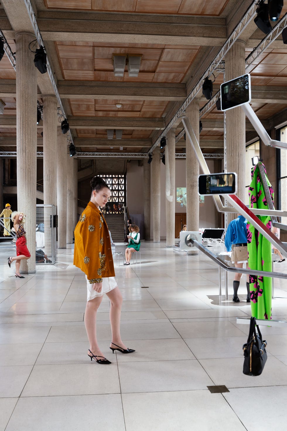 a spacious gallery filled with tall pillars and a polished floor showcases various fashion designs