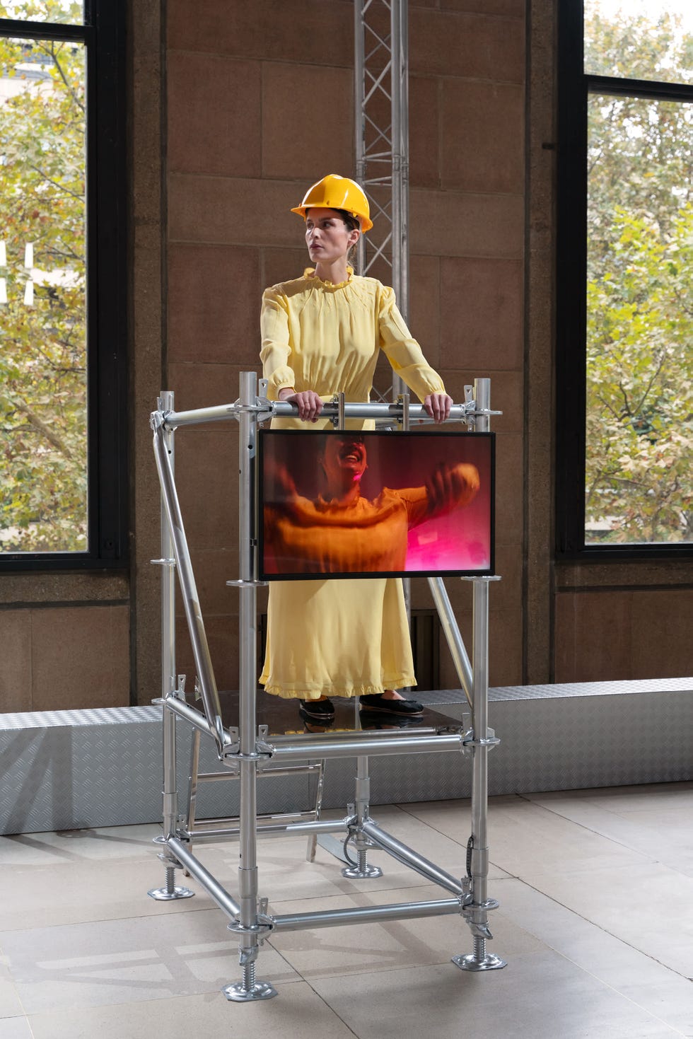 a person wearing a yellow dress and a hard hat stands on a metal scaffolding structure