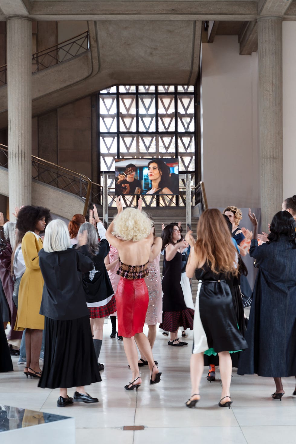 a group of women in fashionable attire are gathered in a spacious indoor area engaged in a lively and celebratory activity
