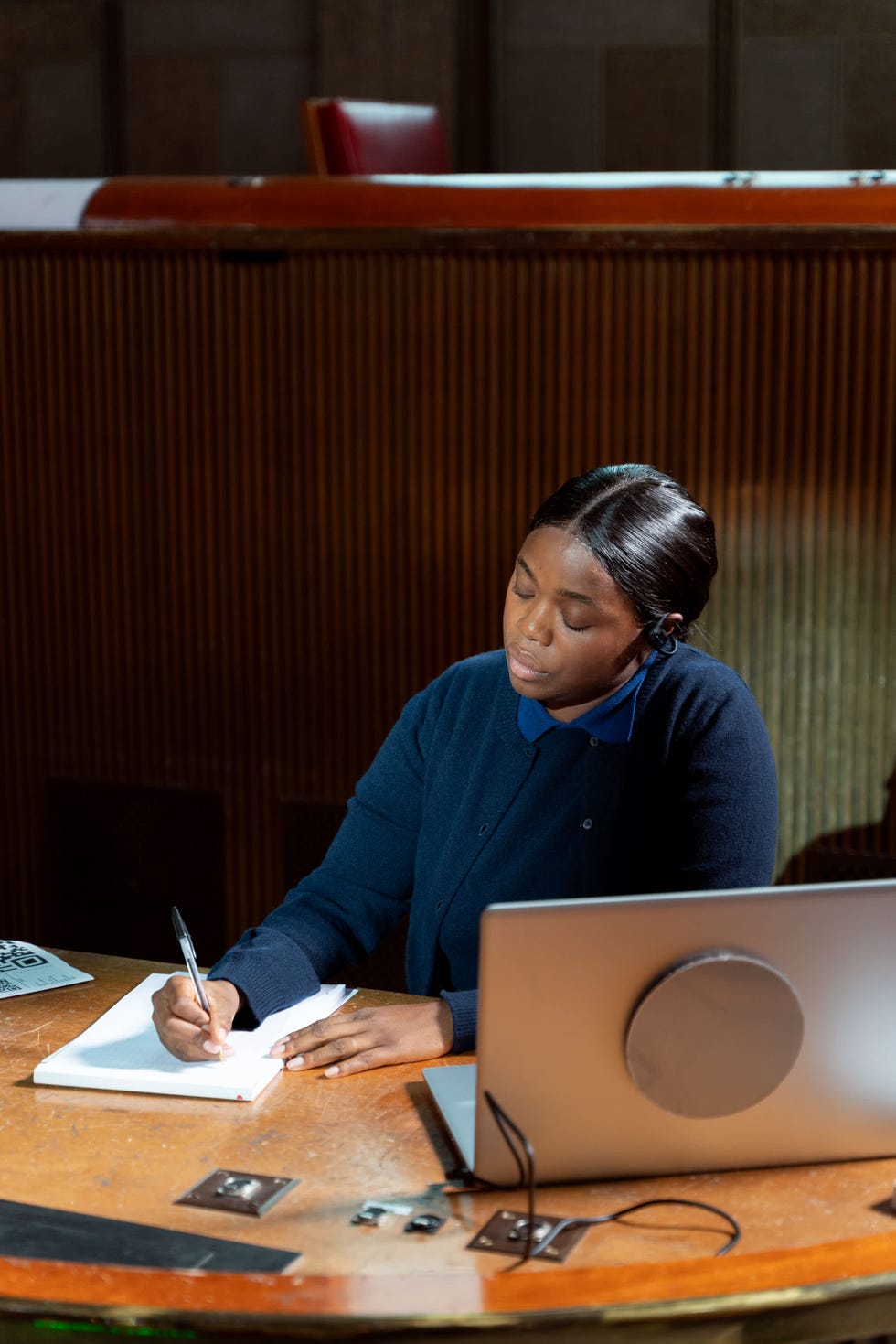 a person is sitting at a wooden desk engaged in writing on a notepad