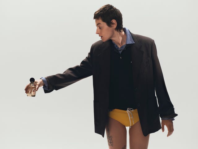 person holding a perfume bottle while dressed in an oversized blazer and athletic shorts