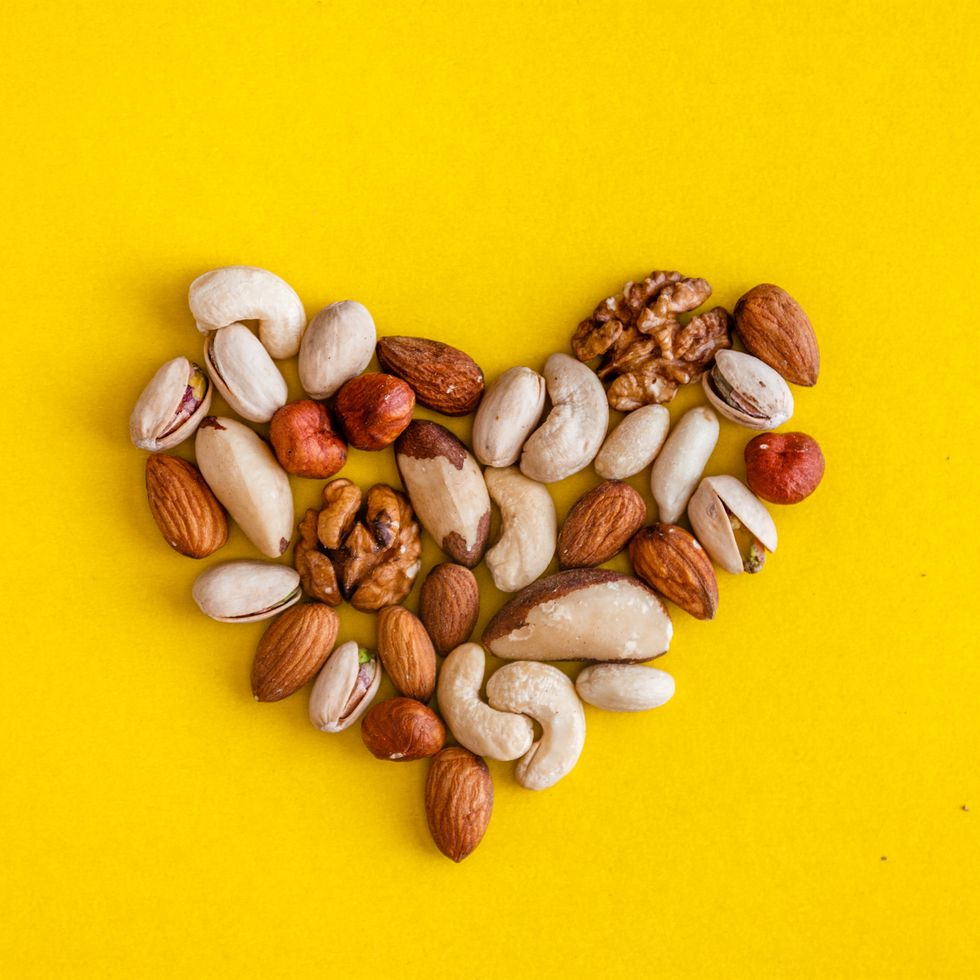 a variety of nuts are laid out in the shape of a heart on a yellow background