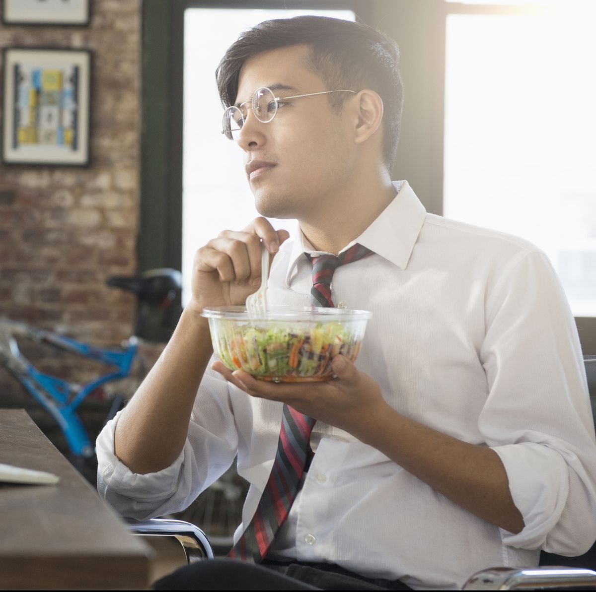 Mixed Race businessman using computer and eating salad at desk