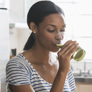 woman drinking glass of green juice in kitchen