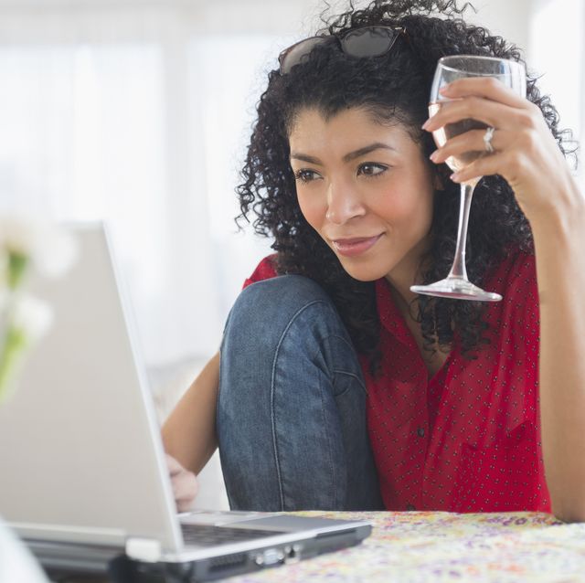 mixed race woman drinking wine and using laptop