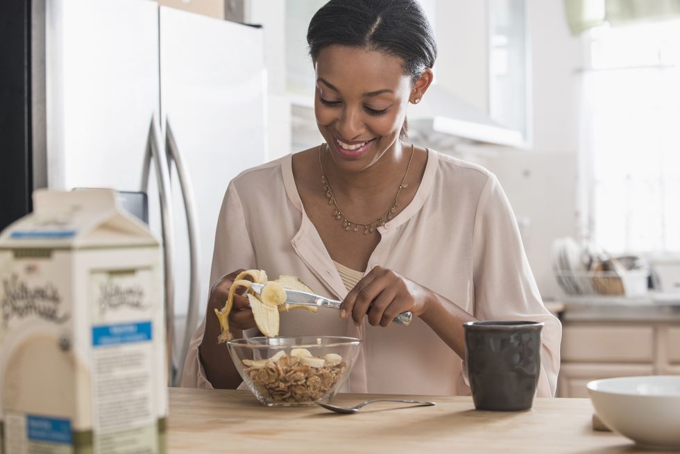 mixed race woman eating cereal and banana in kitchen