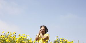 mixed race woman in field of flowers enjoying scent