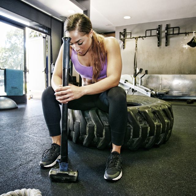 Mixed Race woman resting on tire holding sledgehammer in gymnasium