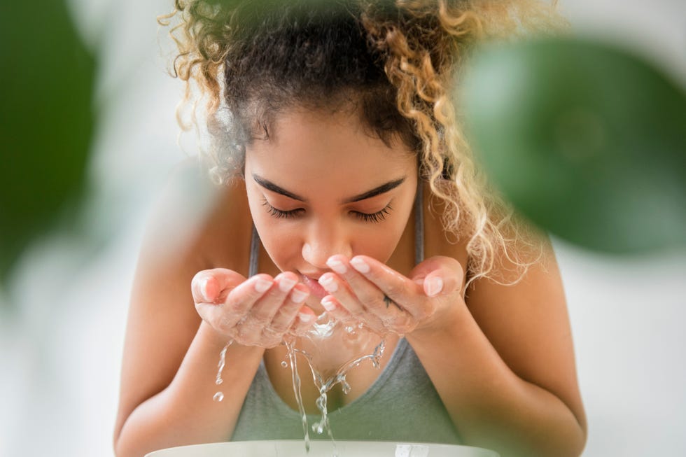 Mixed Race woman splashing water on face