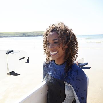mixed race woman with surfboard walking on the be