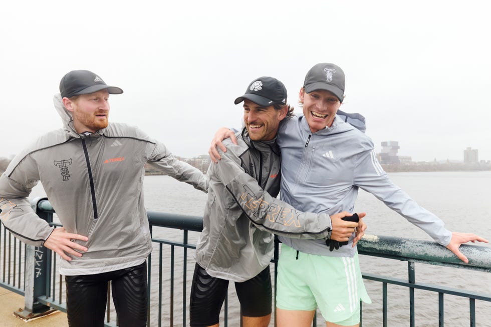 three men wearing running clothes laughing next to a river