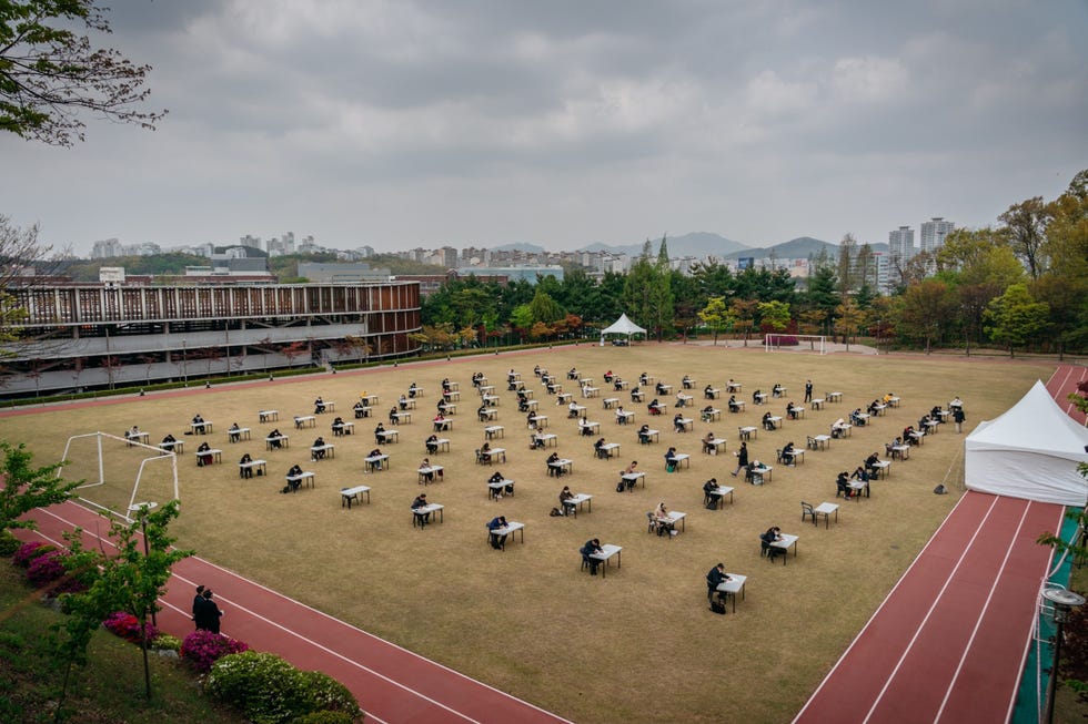 Yongin, South Korea YONGIN ZUIDKOREAAankomende verzekeringsagenten zitten op 25 april 2020 in ZuidKorea verspreid over een voetbalveld achter een bureau om examen te doen De Korea Life Insurance Association en de General Insurance Association of Korea behoorden tot de vele publieke en particuliere instellingen die zich tijdens de pandemie hielden aan de afstandsregels bij examens Er stond die dag veel wind maar er deden in heel Korea meer dan 18000 mensen mee aan het examen voor verzekeringsagent Ze waren blij dat het na twee maanden weer werd gehouden