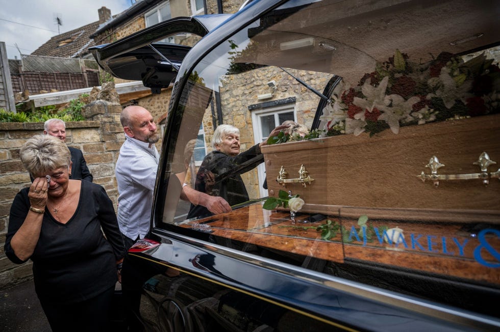 Crewkerne, England CREWKERNE GROOTBRITTANNIFamilieleden leggen bloemen op de kist van Eric Hallett 76 kort voordat hij in een begrafenisauto naar het crematorium van Crewkerne Engeland wordt gebracht 4 mei 2020 Door de voorschriften die wegens de pandemie waren afgekondigd moest het crematorium het aantal rouwenden per begrafenis inperken In plaats daarvan stonden Halletts dierbaren langs de kant van de weg om hem vaarwel te zeggen