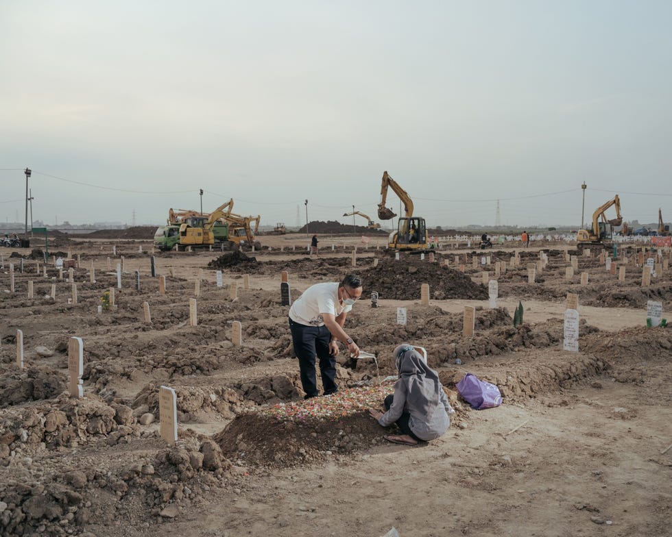 Jakarta, Indonesia JAKARTA INDONESIEIn het noorden van Jakarta bezoeken verwanten het verse graf van een dierbare op de openbare begraafplaats van Rorotan in de wijk Cilincing 21 juli 2021 De begraafplaats is gereserveerd voor COVID19slachtoffers en werd in maart 2021 geopend Hoewel hier 7200 mensen kunnen worden begraven werd de beschikbare ruimte al snel ingenomen door de vele doden die door de opkomst van de Deltavariant in Indonesi werden binnengebracht tijdens de nieuwe golf van besmettingen werd het land een van de epicentra van de pandemie Als noodmaatregel kondigde het stadsbestuur aan dat er meer grondgebied aan de begraafplaats van 25 hectare zou worden toegevoegd