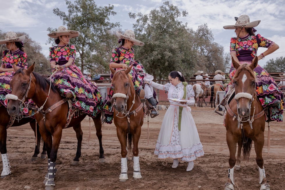 MM9718_210703_004364 Een jurylid inspecteert de kleurige gebloemde kleding van vrouwelijke ruiters escaramuzas tijdens een Mexicaanse rodeo oftewel charreada in de plaats Snelling in Californi De ruiters voeren in amazonezit een complexe synchrone choreografie uit en dragen bloemrijke kleding die zou lijken op de dracht van vrouwen die meevochten tijdens de Mexicaanse revolutie Hun jurken worden al even streng beoordeeld als hun rijkunsten elke afwijking van de strikte regels leidt tot puntenaftrek