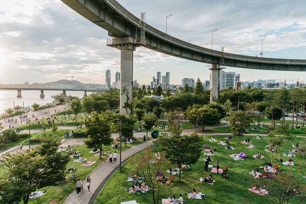 SEOUL ZUIDKOREAInwoners van Seoul zitten in een weekend aan het eind van de zomer van 2021 op picknickkleedjes op het gras in het Ttukseom Hangang Park Het park dat onder een ringweg ligt die leidt naar een brug en een snelweg is een populaire plek voor jong en oud
