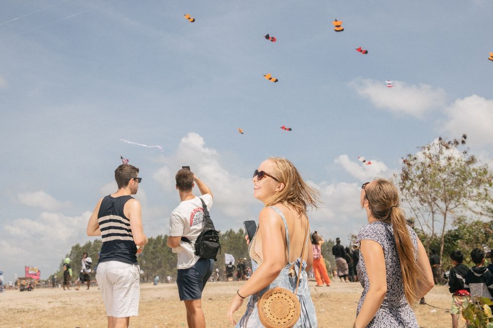 Toeristen kijken hoe vliegers worden opgelaten tijdens het Bali Kite Festival dat dit jaar weer werd gehouden na enkele jaren te zijn afgelast vanwege de COVID19pandemie Aan de wedstrijd doen zowel eilandbewoners als buitenlanders mee