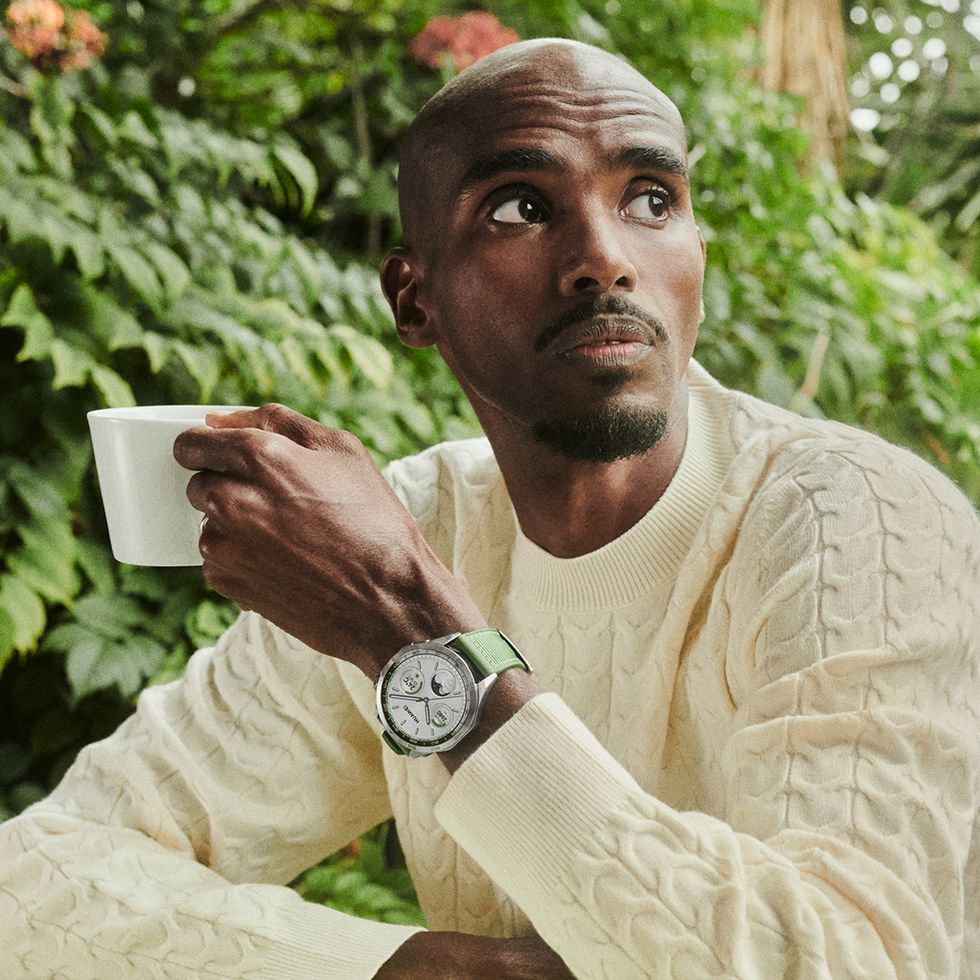 mo farah wearing a cream cable knit jumper and a huawei watch, holding a mug and looking off to the distance