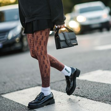 paris, france   september 29 a guest wears a black sweater, a black pleated  accordion skirt, brown ff embroidered monogram pattern tights from fendi, a black shiny leather jacquemus handbag, white ribbed socks, black shiny leather prada loafers  shoes, outside acne studios , during paris fashion week   womenswear spring summer 2022, on september 29, 2021 in paris, france photo by edward berthelotgetty images