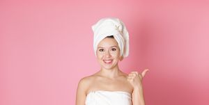 mock up smiling young woman in towel pointing finger at free space for text isolated on pink background