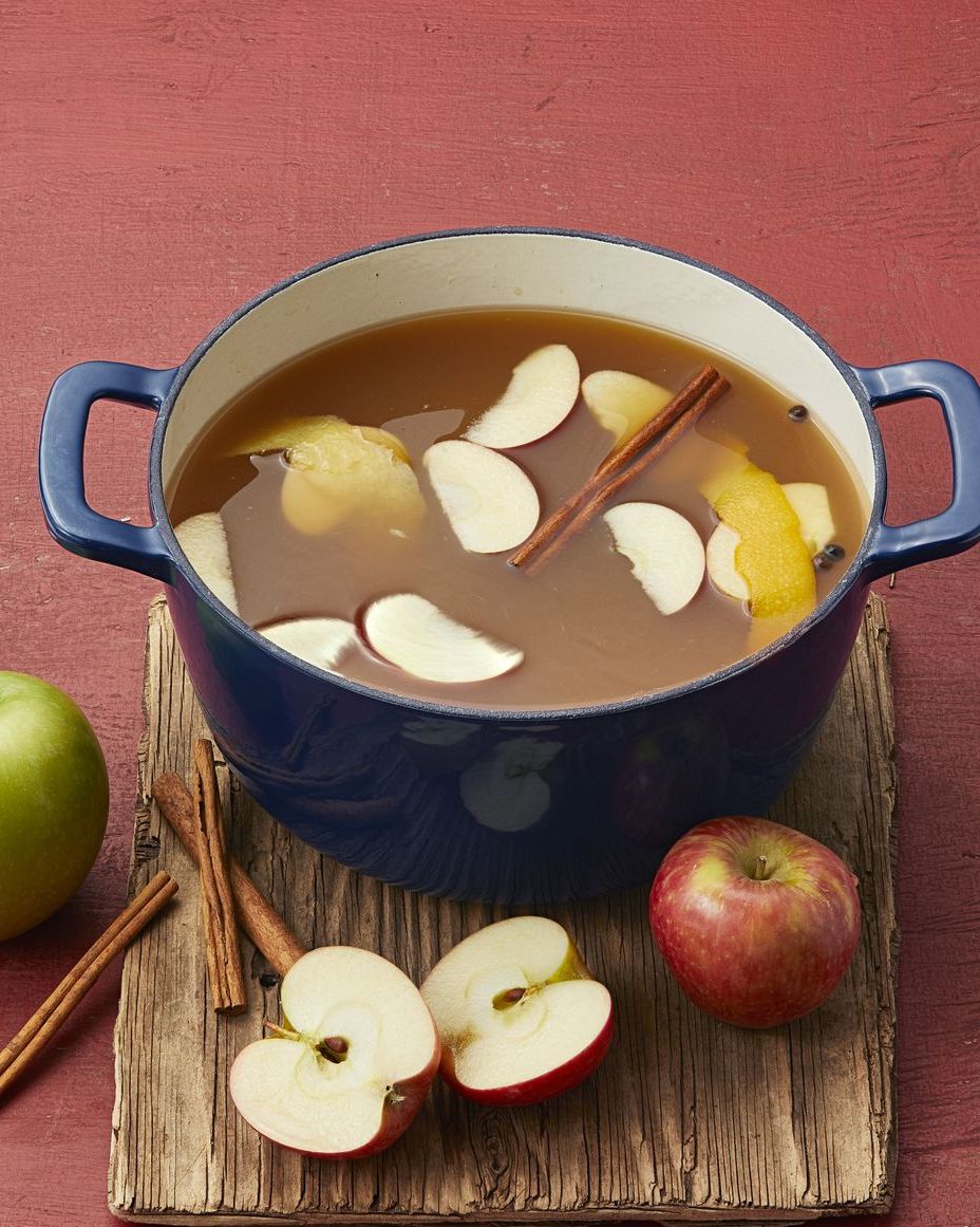 mulled apple cider in dutch oven on wood board with apples and cinnamon