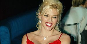 anna nicole smith smiles at the camera, she is wearing a low cut red dress with sequin embellishments, heart shaped sparkly earrings, and a silver necklace, her hair is styled up and she has on heavy makeup